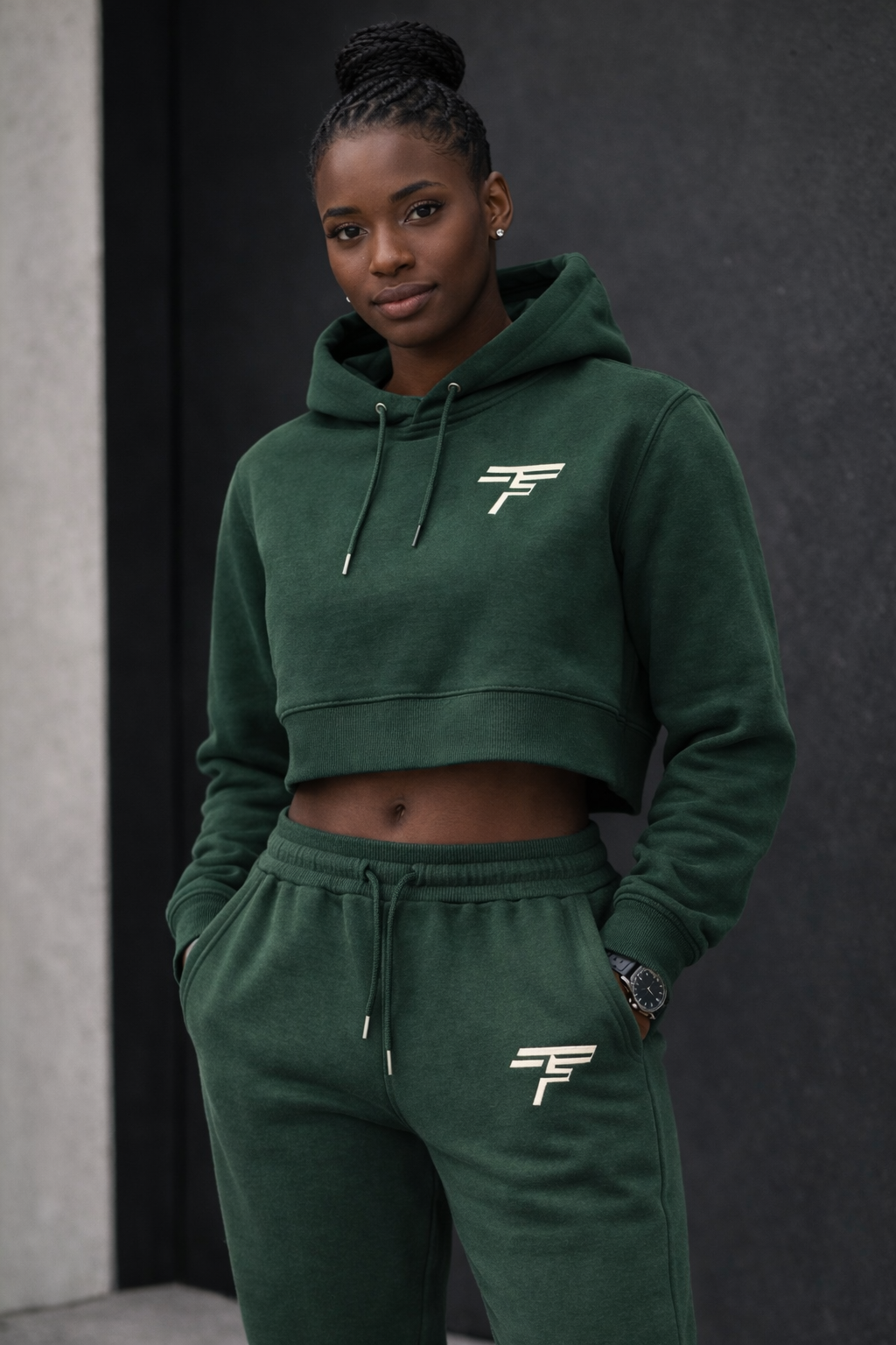 Person wearing a green hoodie and pants with a logo, standing against a dark background.