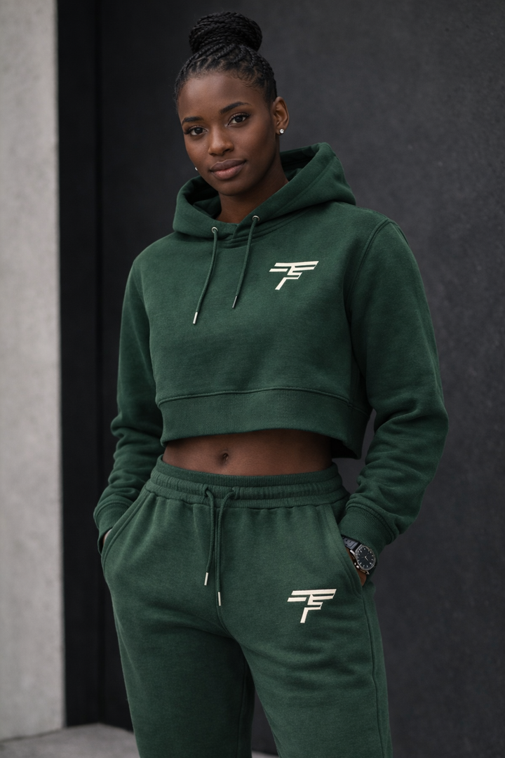 Person wearing a green hoodie and pants with a logo, standing against a dark background.